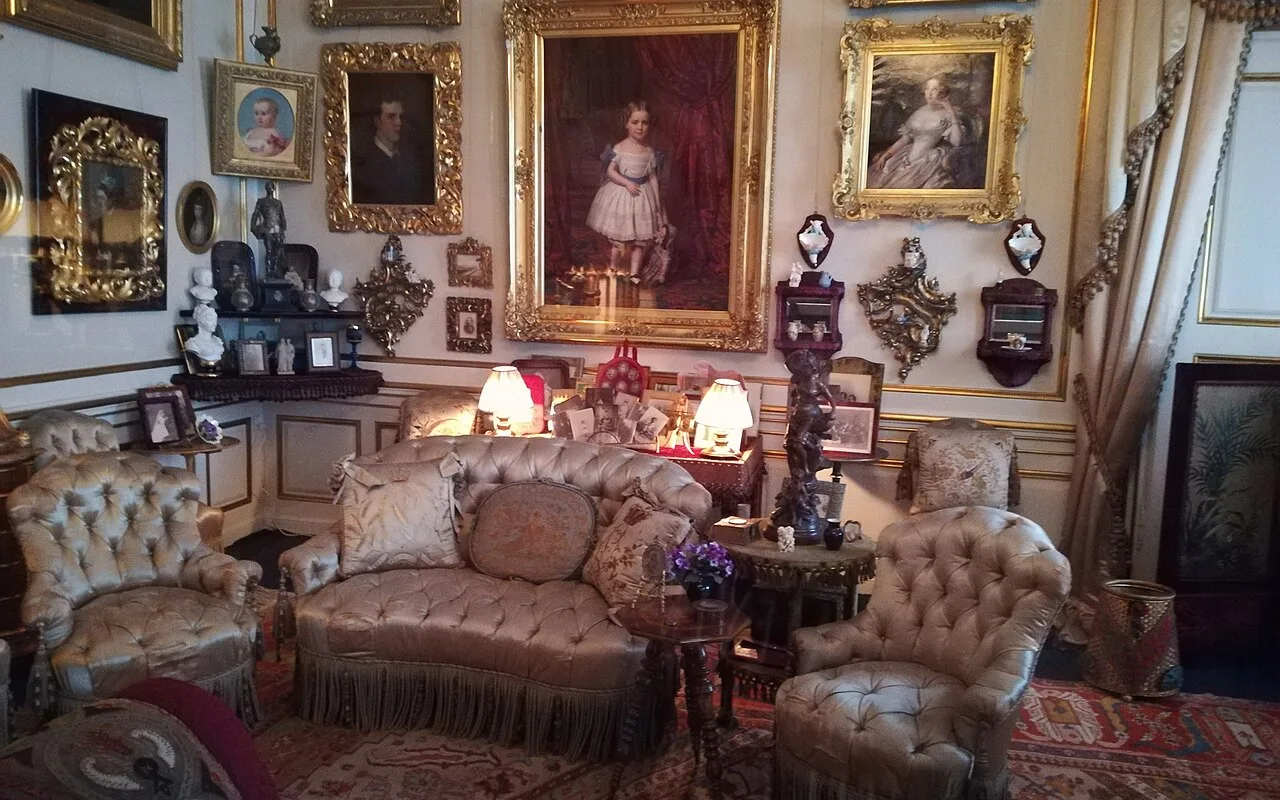 En salon på Amalienborgmuseet med forgyldte familiportrætter i rammer over knappede silkestole og en sofa med frynser.